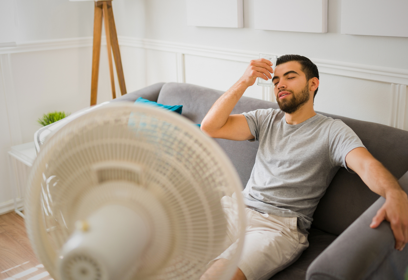 Man cooling off with a fan while waiting for AC repair in Athens, AL